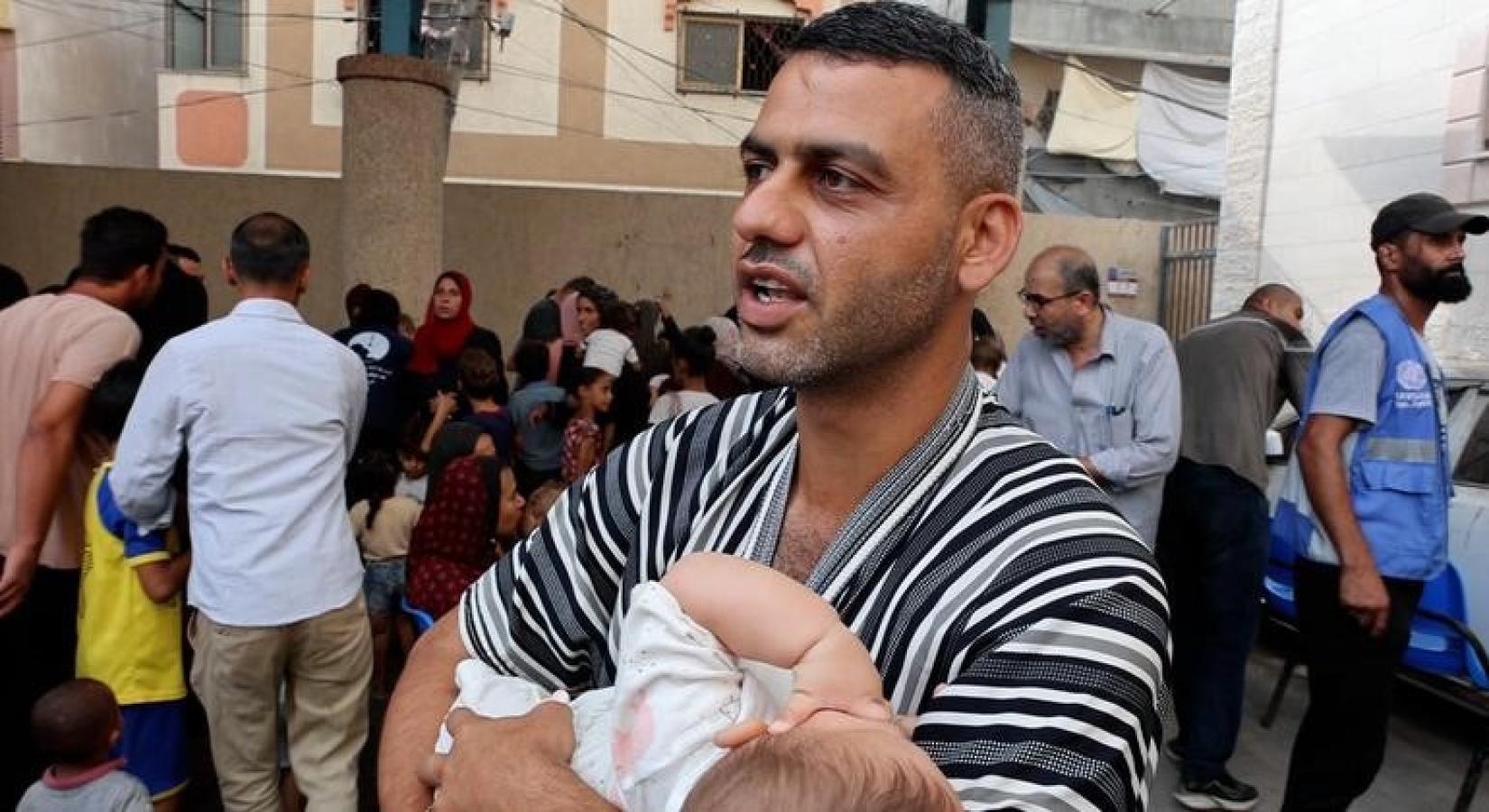 A man holds a baby, there are several people behind him.