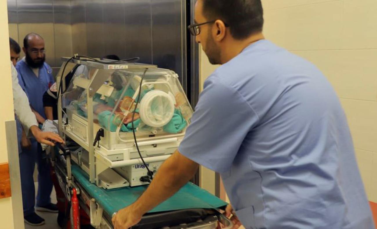 Health personnel is pushing babies in incubators to an elevator.