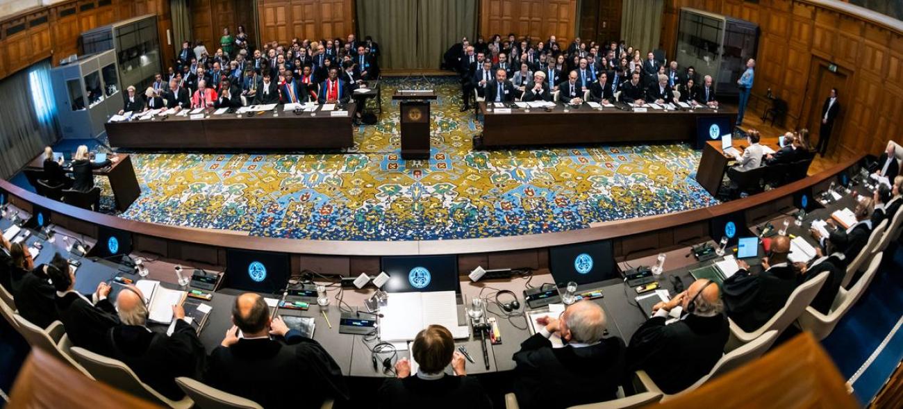 Uluslararası Adalet Divanı'nın içi. Yargıçlar üstte, avukatları ve izleyicilerle karşı karşıya görülüyor. Salon güzel bir halı ile kaplı.. 