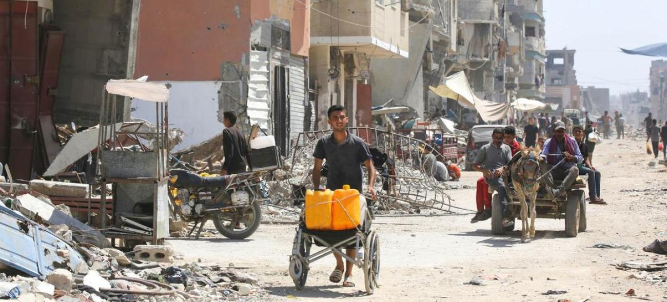 One man pushing a hand made looking cart, behind him a horse carriage on a destroyed street in Gaza