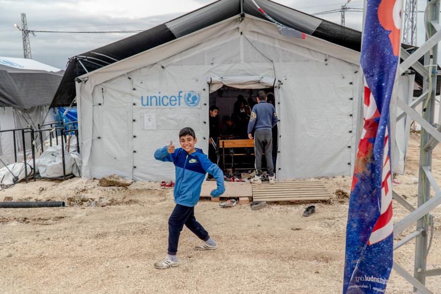 A tent with UNICEF written on it and a child says hi to the camera