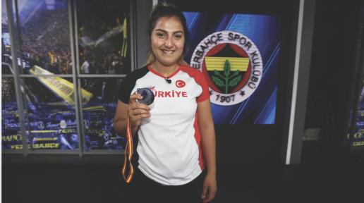 Üzerinde Türkiye yazan t-shirtü ile Eda Tuğsuz Fenerbahçe Spor Kulübü arması önünde madalyasını göstererek poz vermiş 