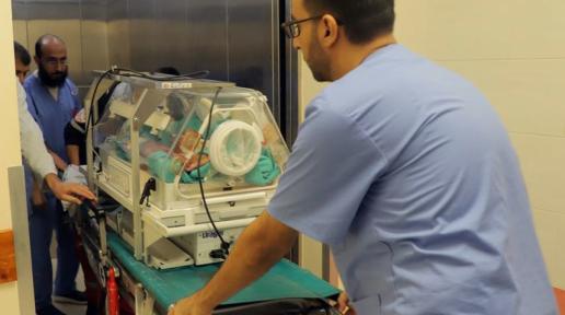 Health personnel is pushing babies in incubators to an elevator.